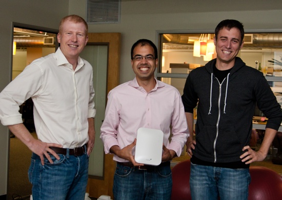 Three men smiling holding a device