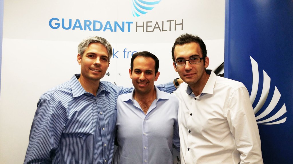 Three men in front of a Guardant Health logo