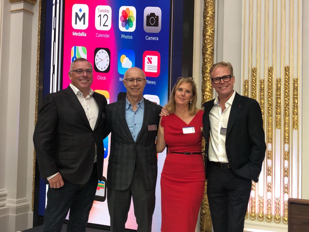 Four people stand in front of a large iPhone display